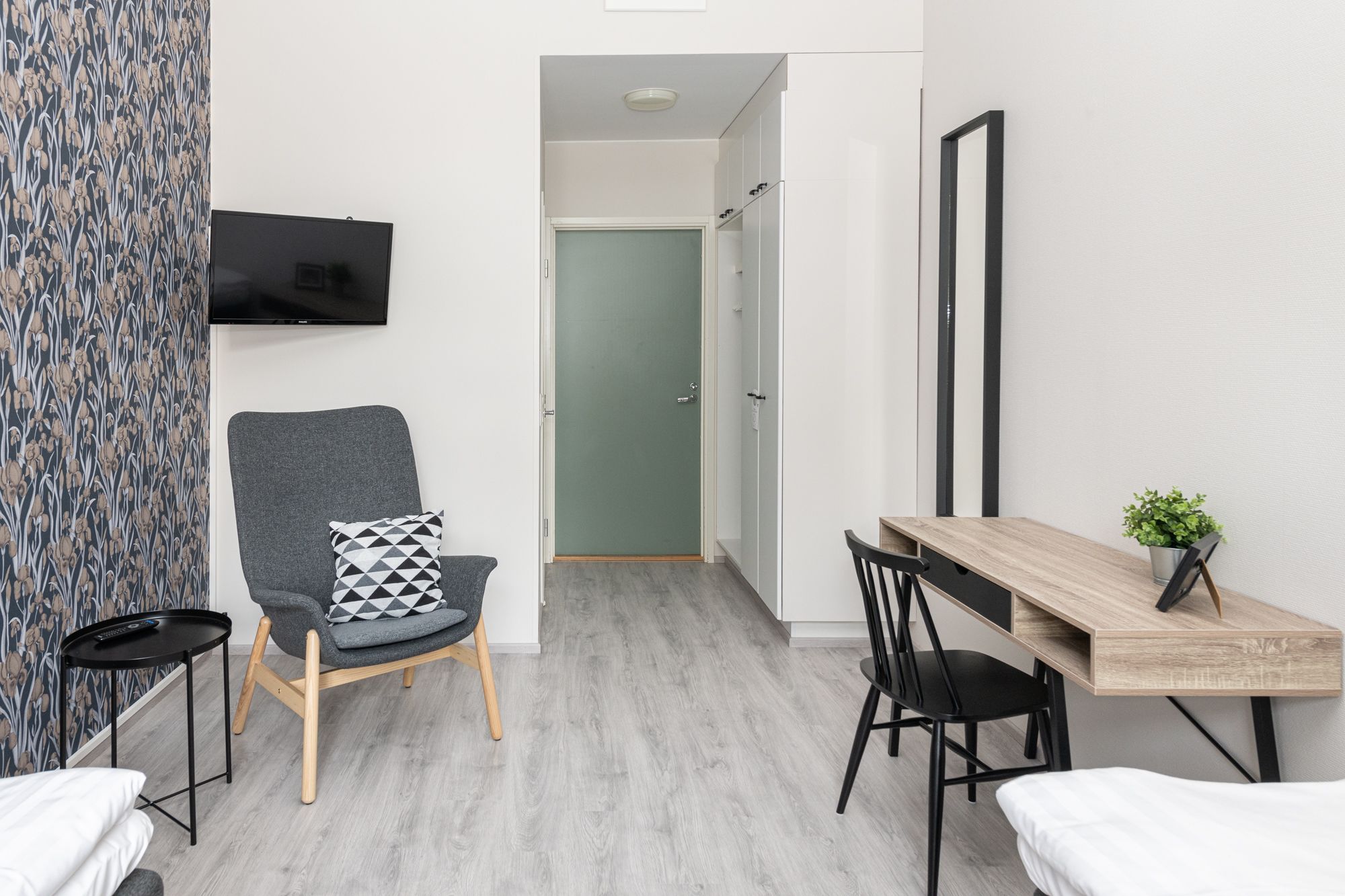 Una habitación moderna con un sillón gris, una mesa de comedor de madera y un televisor montado en la pared.