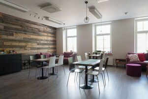 Un comedor moderno con una pared de acento de madera, una mesa de comedor con sillas, y una zona de estar con sofá y reposapiés.