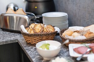 Un bufé de desayuno con pan, bollos y un bol de yogur.