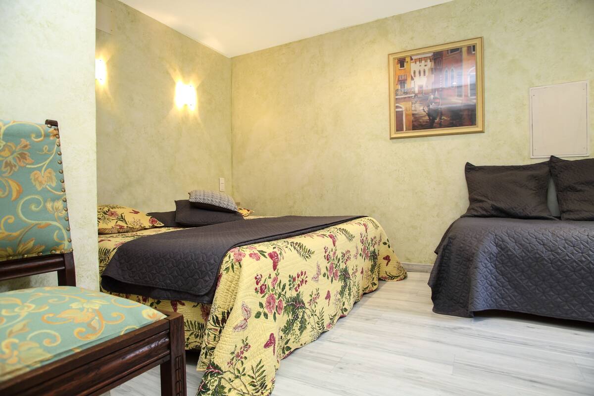 Une chambre avec deux lits, des couvre-lits à motifs floraux, une chaise et un tableau au mur.