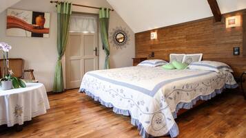 Een slaapkamer met een houten plafond, een bed met een bloemenprintdeken, een nachtkastje met een bloempot en een spiegel aan de muur.