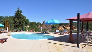 A swimming pool with lounge chairs and umbrellas, surrounded by trees and a clear sky. - Lo Gorissado - La Ferme du Glandier (Saint-Andre-d'Allas)