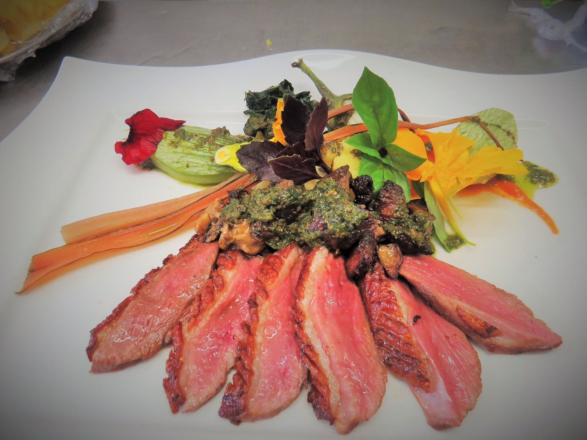 A plate of food with sliced meat, vegetables, and a green sauce.