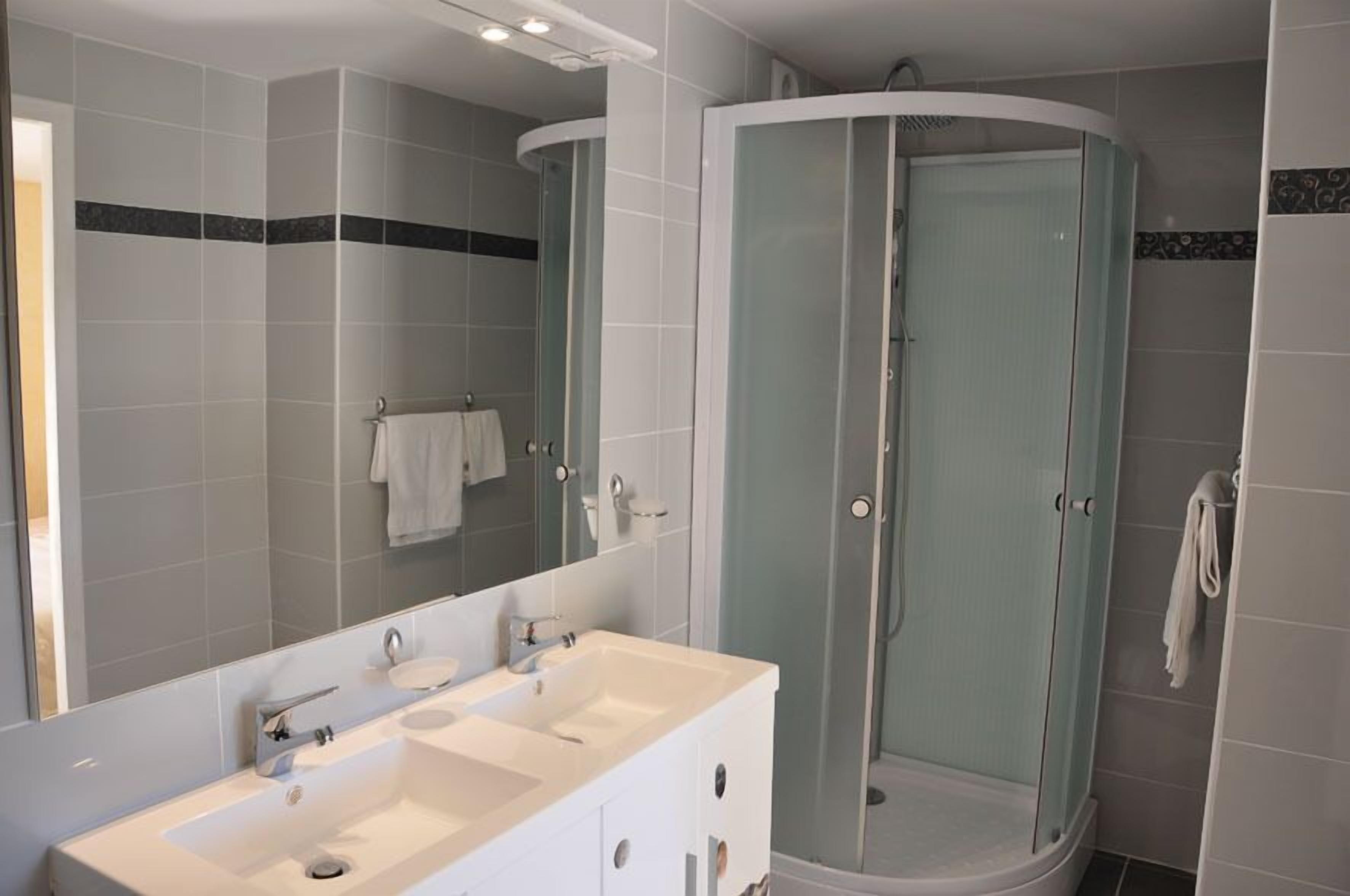 A modern bathroom with a double sink vanity, a glass-enclosed shower, and a large mirror.