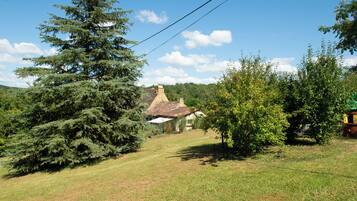 Une maison de campagne avec un toit de chaume, entourée d’arbres et d’un champ herbeux.