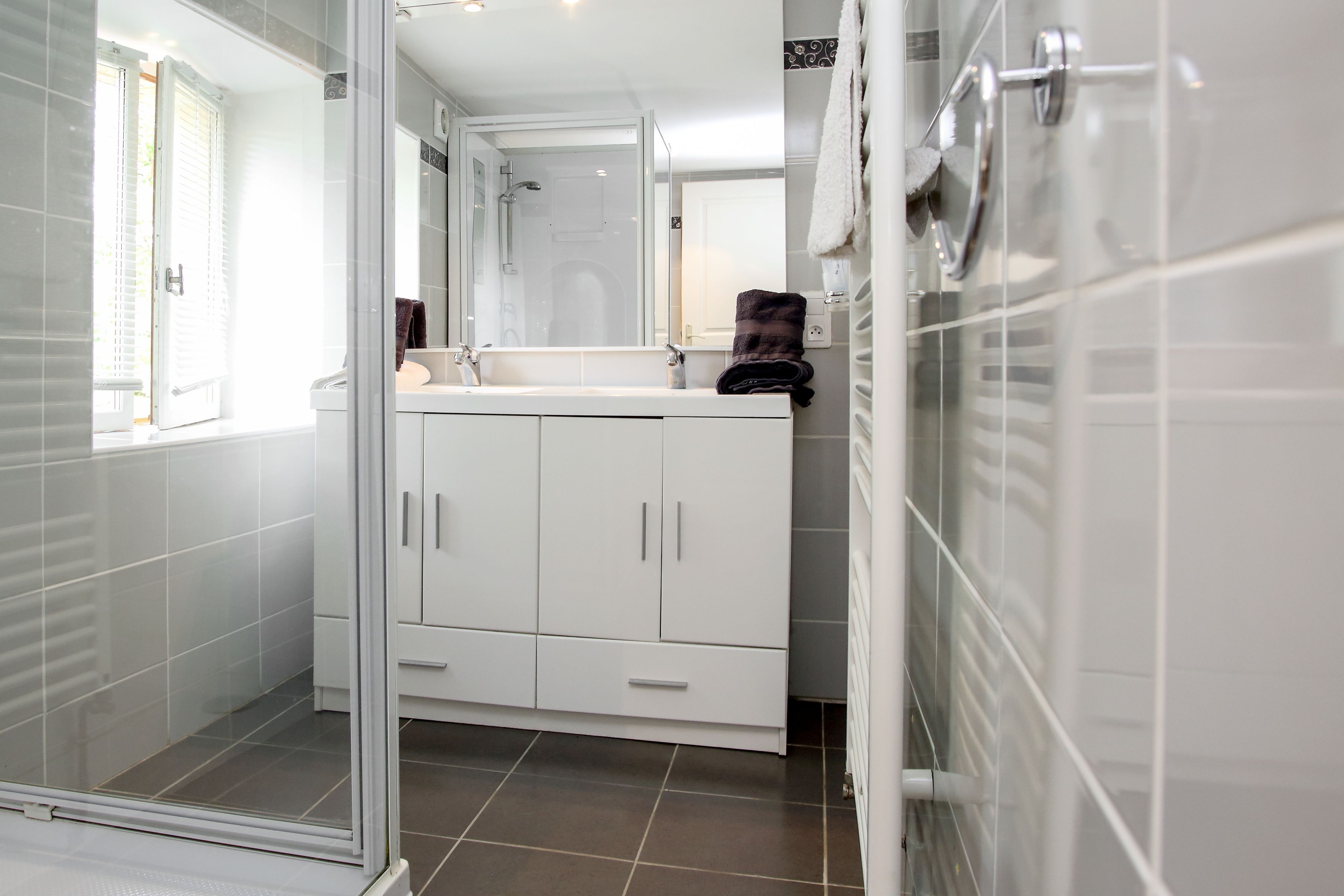 Un baño moderno con armarios blancos, cabina de ducha de vidrio y ventana que proporciona luz natural.
