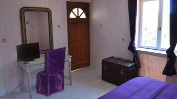 Un dormitorio con una cama, un escritorio con computadora, un tocador, un espejo, una puerta y una ventana con cortinas.
