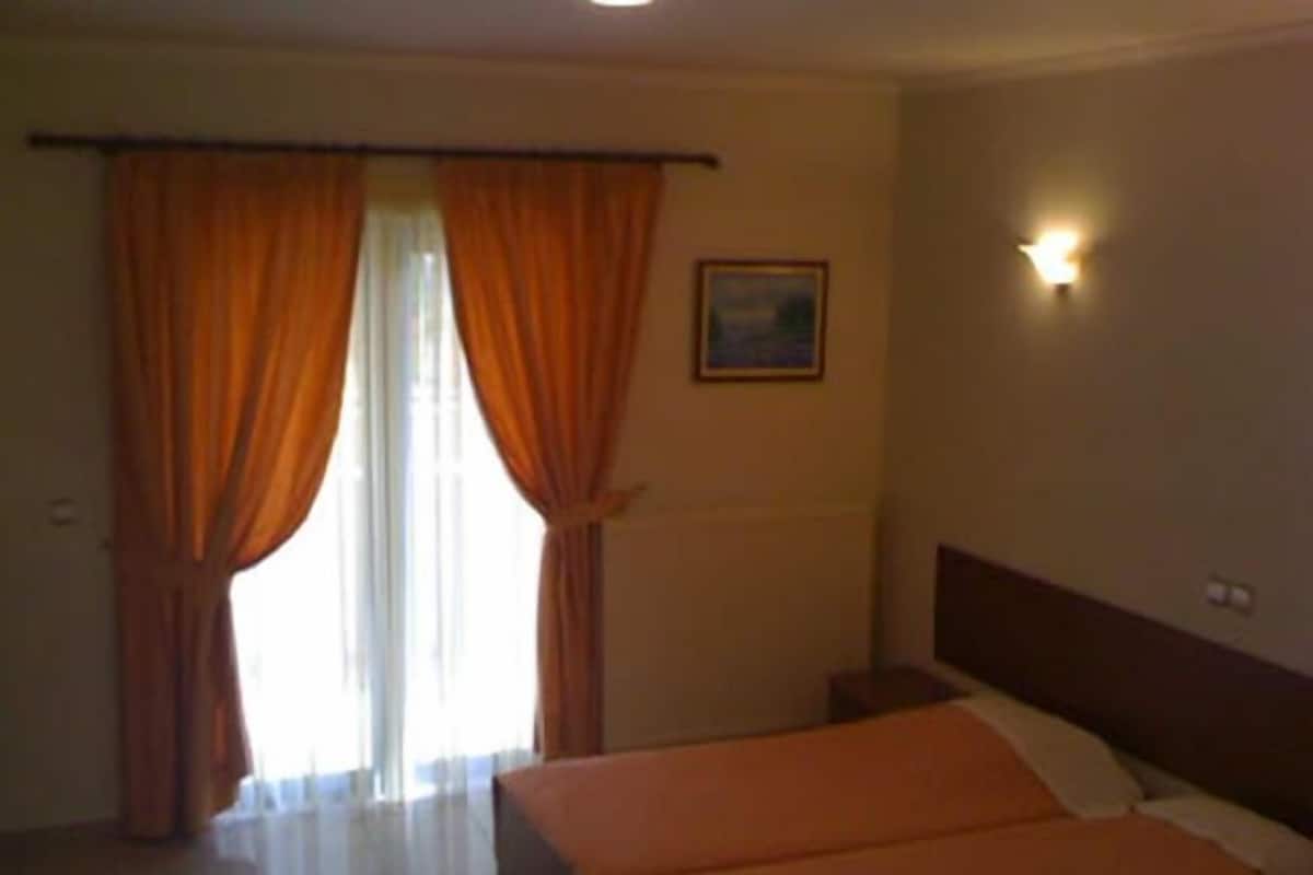A hotel room with two beds, a painting on the wall, and a window with curtains.