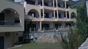 A multi-story hotel with balconies, a stone staircase, and a mountainous backdrop. - J Studios (Megara)