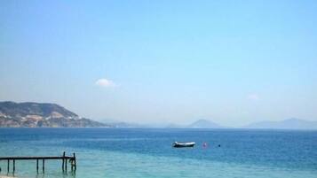 A beach with a wooden pier extending into calm waters, a small boat, and distant hills under a clear sky.