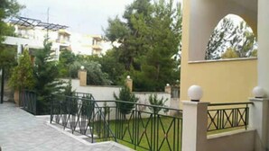 A residential area with a paved walkway, green lawn, and a yellow building with a balcony. - J Studios (Megara)