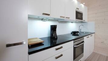 Una cocina moderna con armarios blancos, encimera negra, microondas, cafetera y horno.