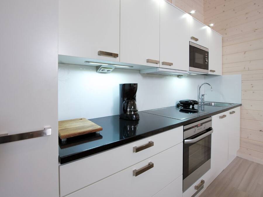 Una cocina moderna con armarios blancos, encimera negra, microondas, cafetera y horno.