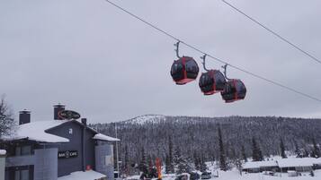En skilift med gondoler, en bygning med skilt til bar og café, og et sneklædt bjerg i baggrunden.