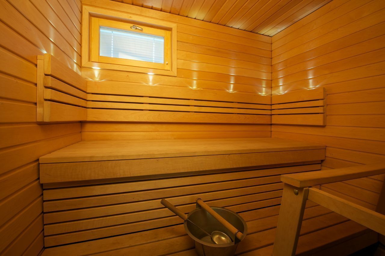 Una sauna con paredes de madera, un banco, una ventana y un balde.
