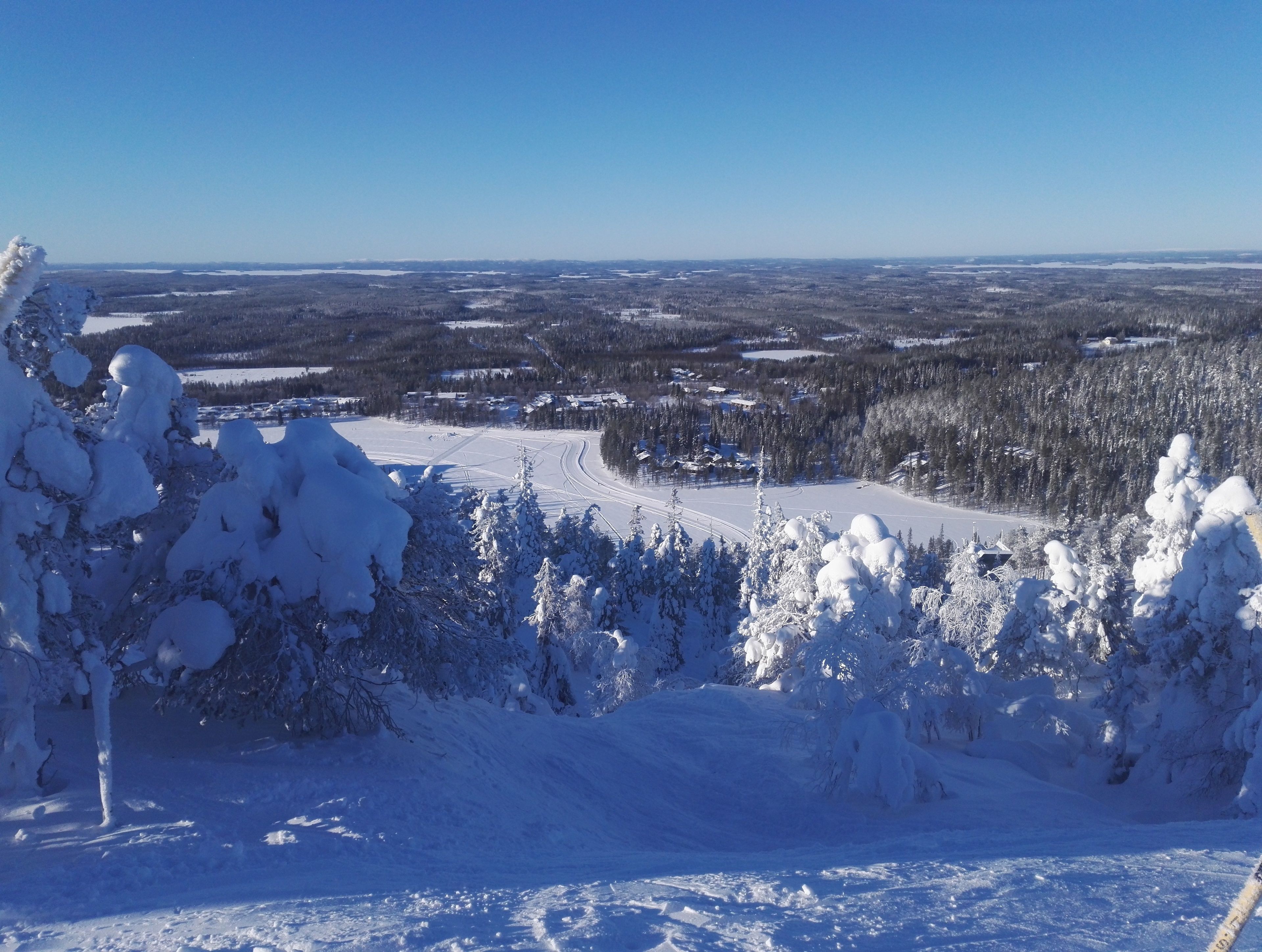 Schneebedeckte Landschaft mit freiem Blick auf einen Skiort, einschließlich Skipisten und einem bewaldeten Gebiet.