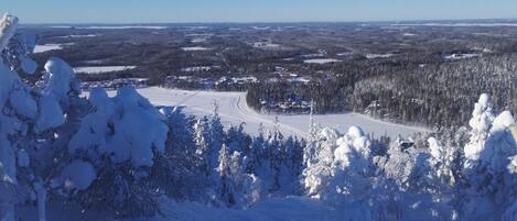 Schneebedeckte Landschaft mit freiem Blick auf einen Skiort, einschließlich Skipisten und einem bewaldeten Gebiet.