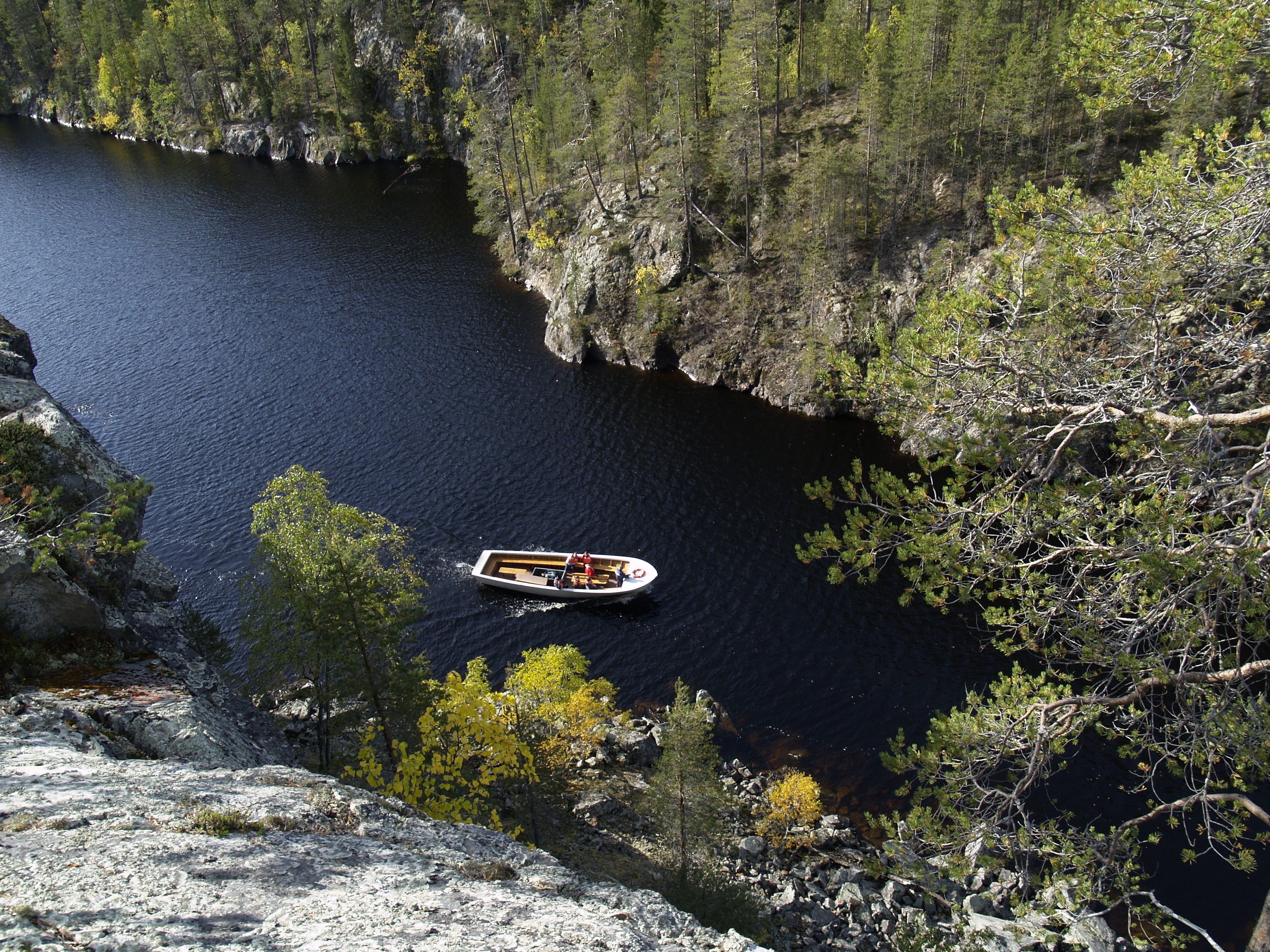 Un bote en un río tranquilo rodeado de acantilados rocosos y un bosque denso.