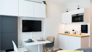 A compact kitchenette with a microwave, oven, and sink. There is a dining area with a table and chairs, and a flat-screen TV mounted on the wall. - WE Apartments (Warsaw)