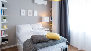 A modern bedroom with a bed, bedside table, lamp, and a bookshelf. - WE Apartments (Warsaw)