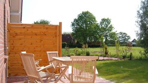 Eine Terrasse mit Holztisch und -stühlen, einem Pflasterboden und einem Holzzaun.