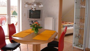 Ein Essbereich mit Tisch, Stühlen, einem Fernseher und einer Blumenvase.