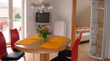 A dining area with a table, chairs, a TV, and a flower vase.
