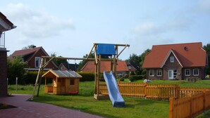 Ein Spielplatz mit Rutsche, Schaukeln und einer kleinen Holzkonstruktion.