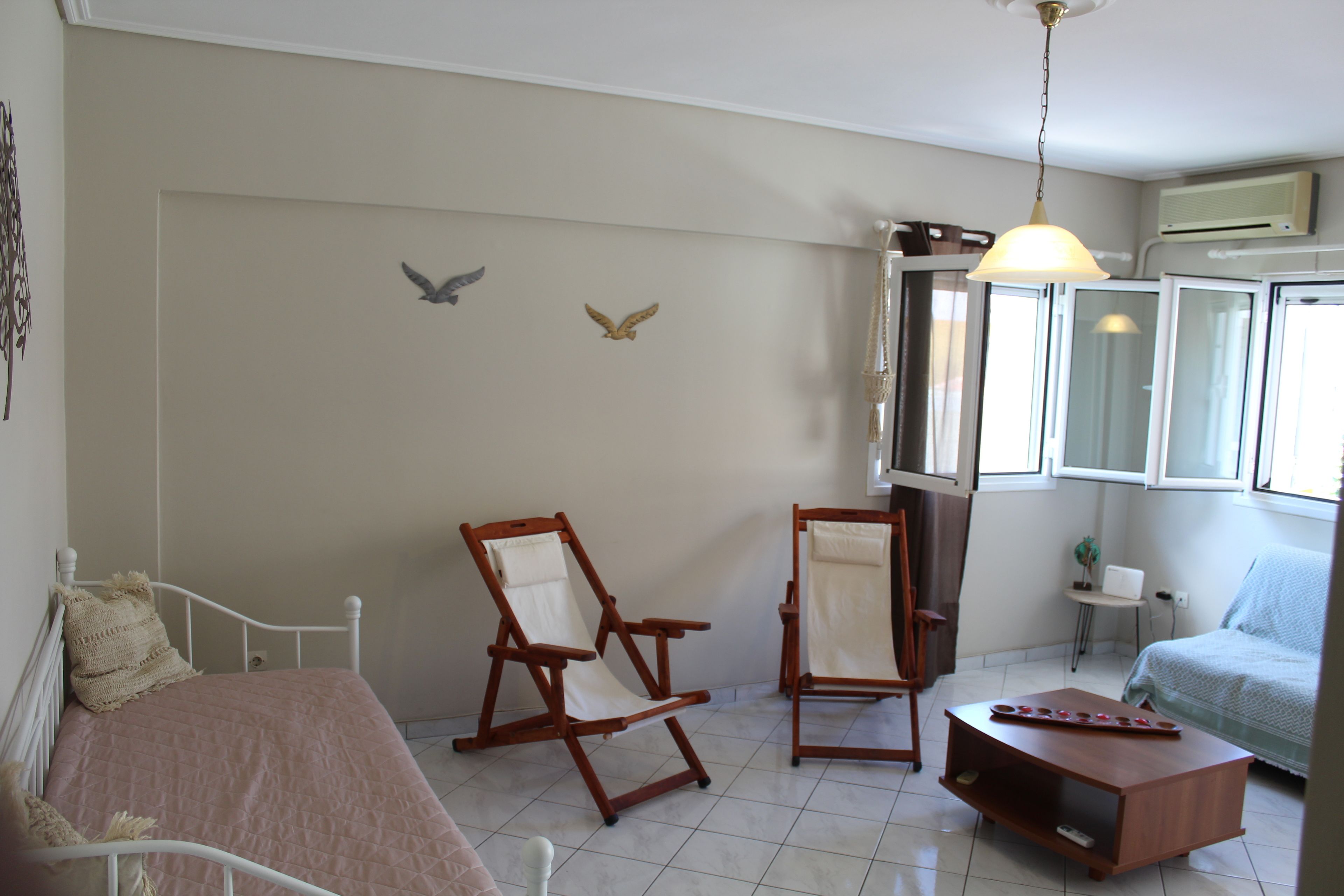 A room with a bed, two rocking chairs, a small table, and a window with an air conditioner.