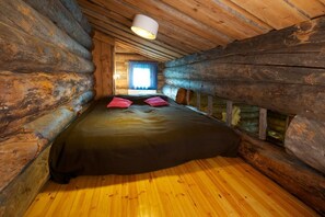 Un dormitorio tipo cabaña de madera con cama, almohadas y ventana con cortinas.
