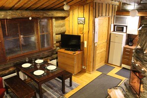 Interior acogedor de una cabaña con una mesa de comedor de madera preparada para cuatro personas, un televisor, un refrigerador y un microondas.