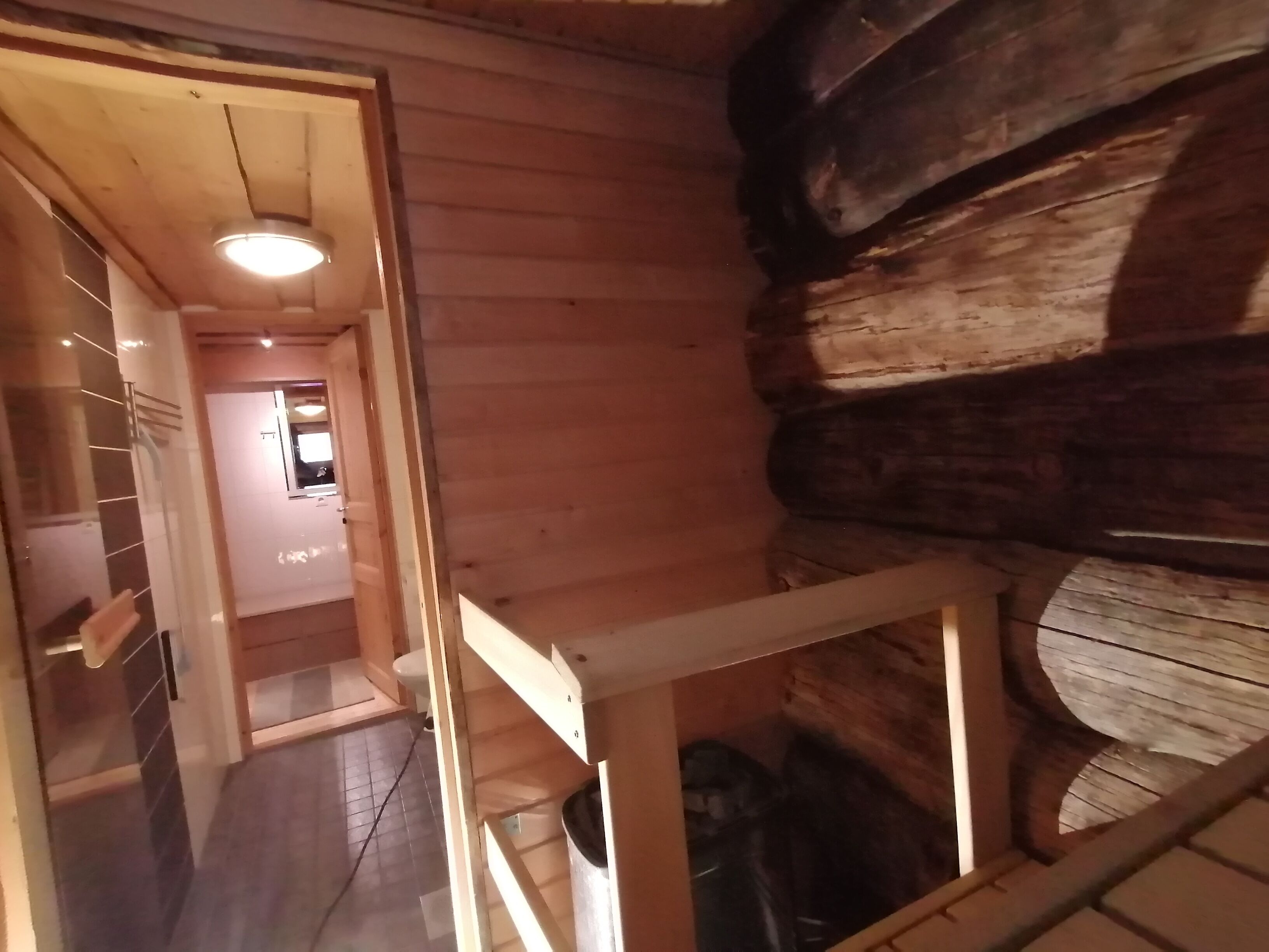 A wooden interior with a staircase leading to a second floor. A hallway with a tiled floor and a door to a bathroom is visible.