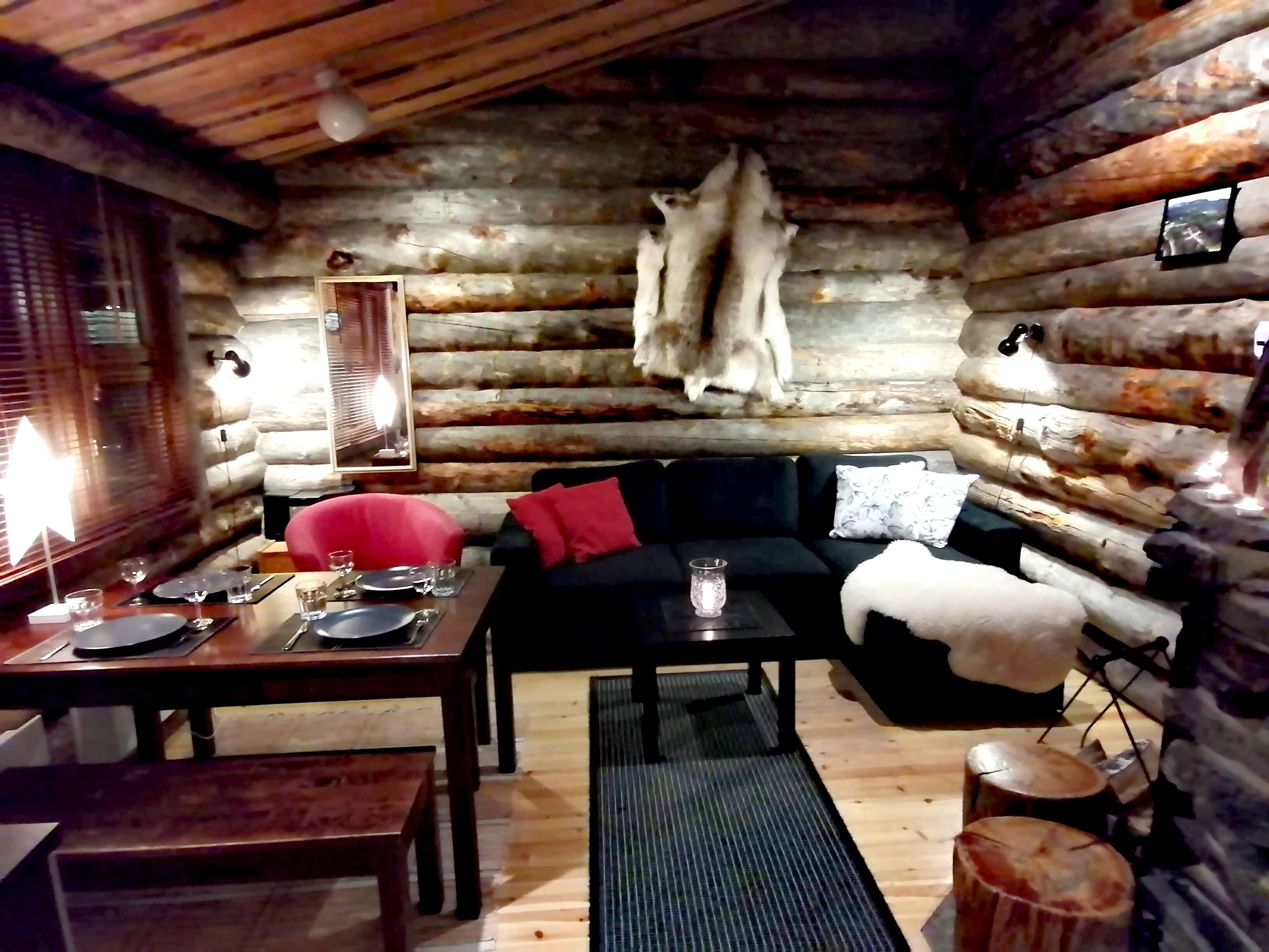 A log cabin interior with a dining area, sofa, and a mounted animal hide.