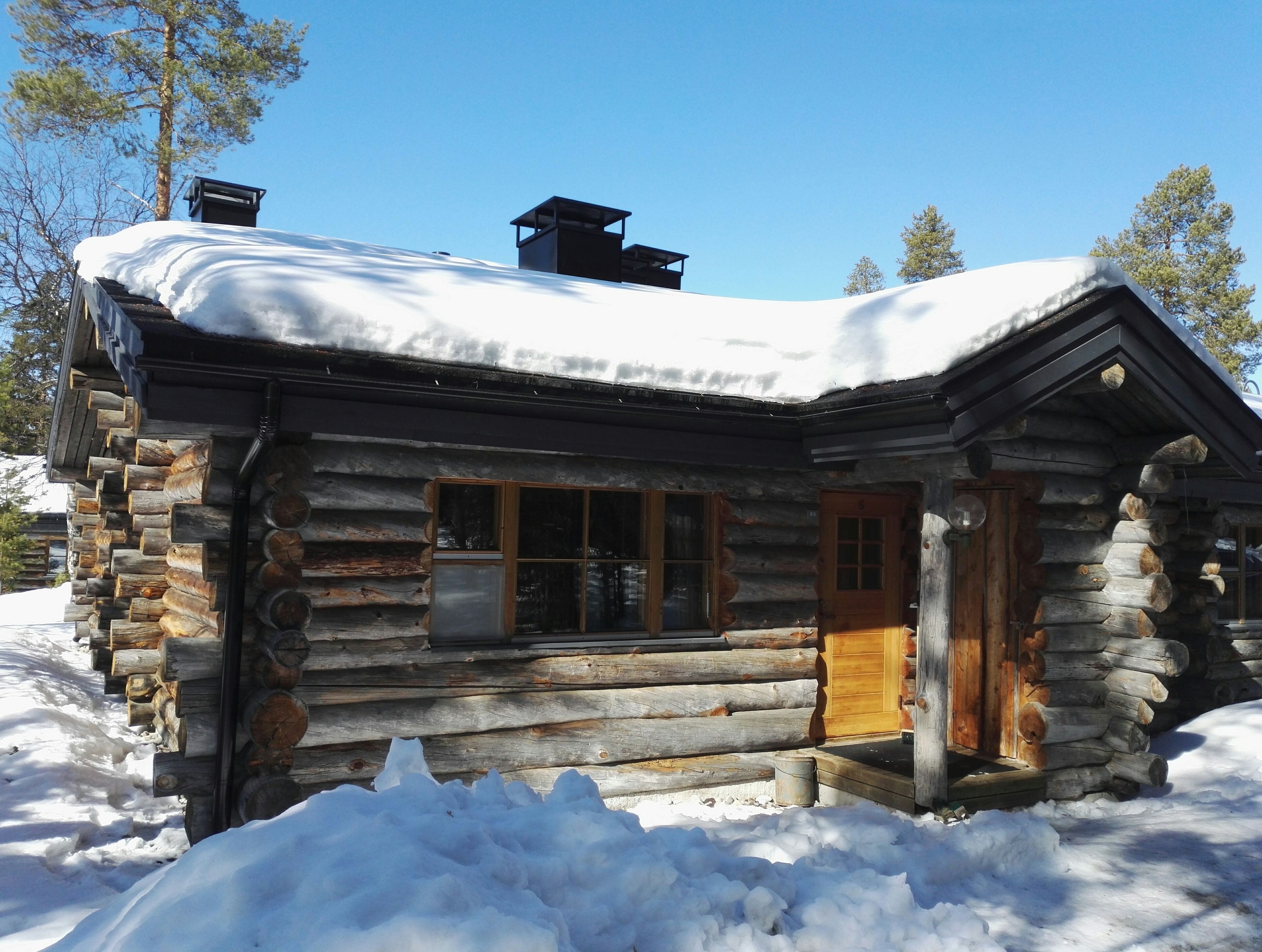 Una cabaña de madera con puerta y ventanas, rodeada de nieve.