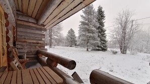 Una cabaña de troncos con una mesa de madera y bancos, un paisaje nevado con árboles y una vista despejada al exterior.