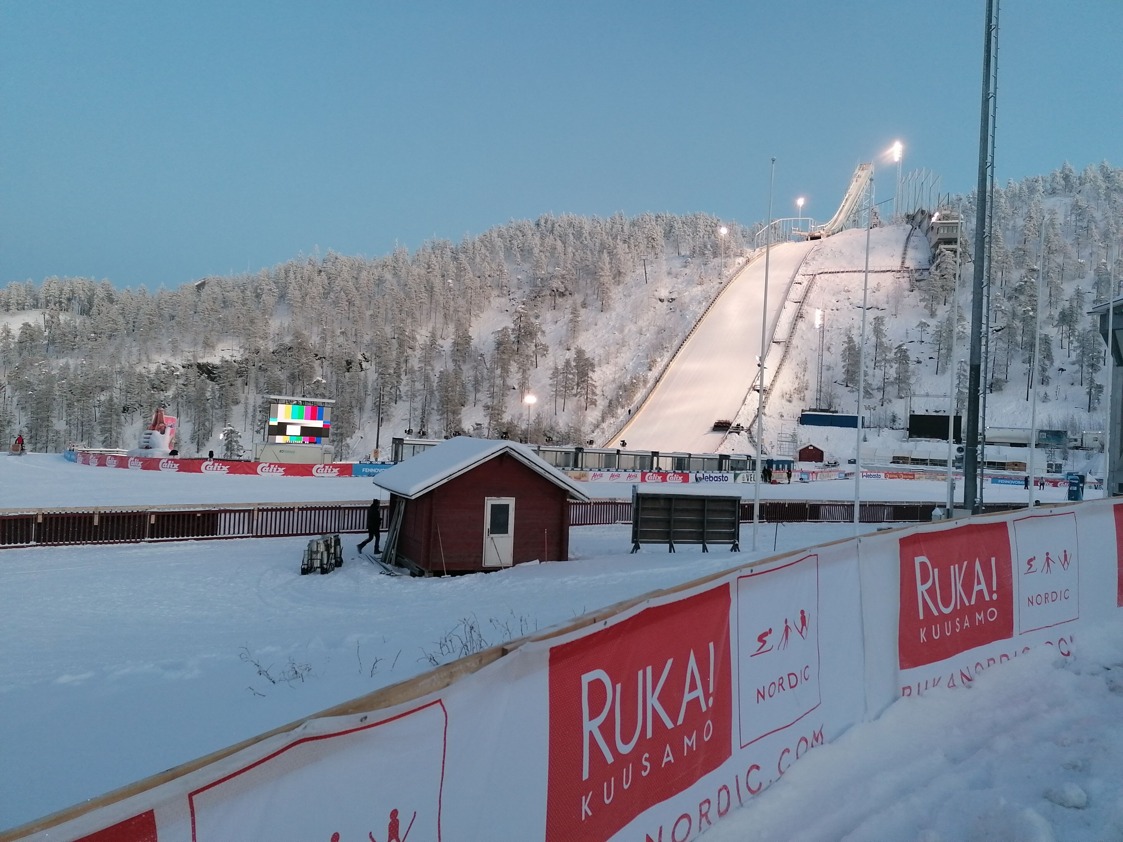 A snowy ski slope with a small cabin and a ski lift in the background.