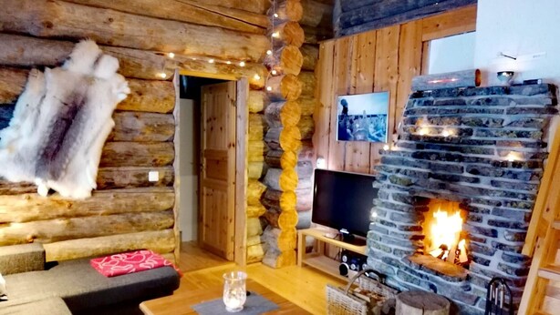 Un acogedor interior de cabaña de madera con chimenea de piedra, mobiliario de madera y un televisor.
