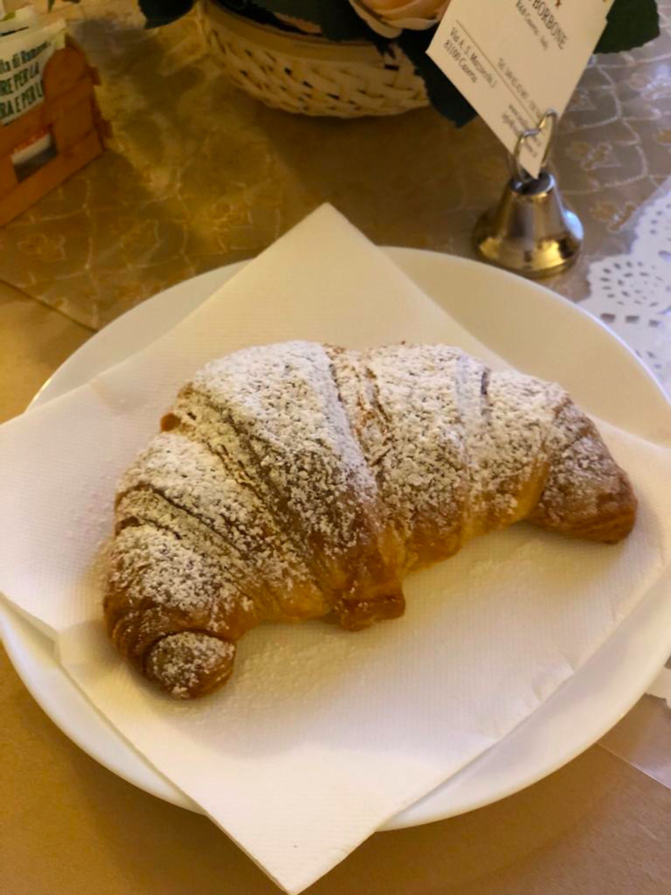 Un croissant sobre un plato blanco, cubierto de azúcar glas.
