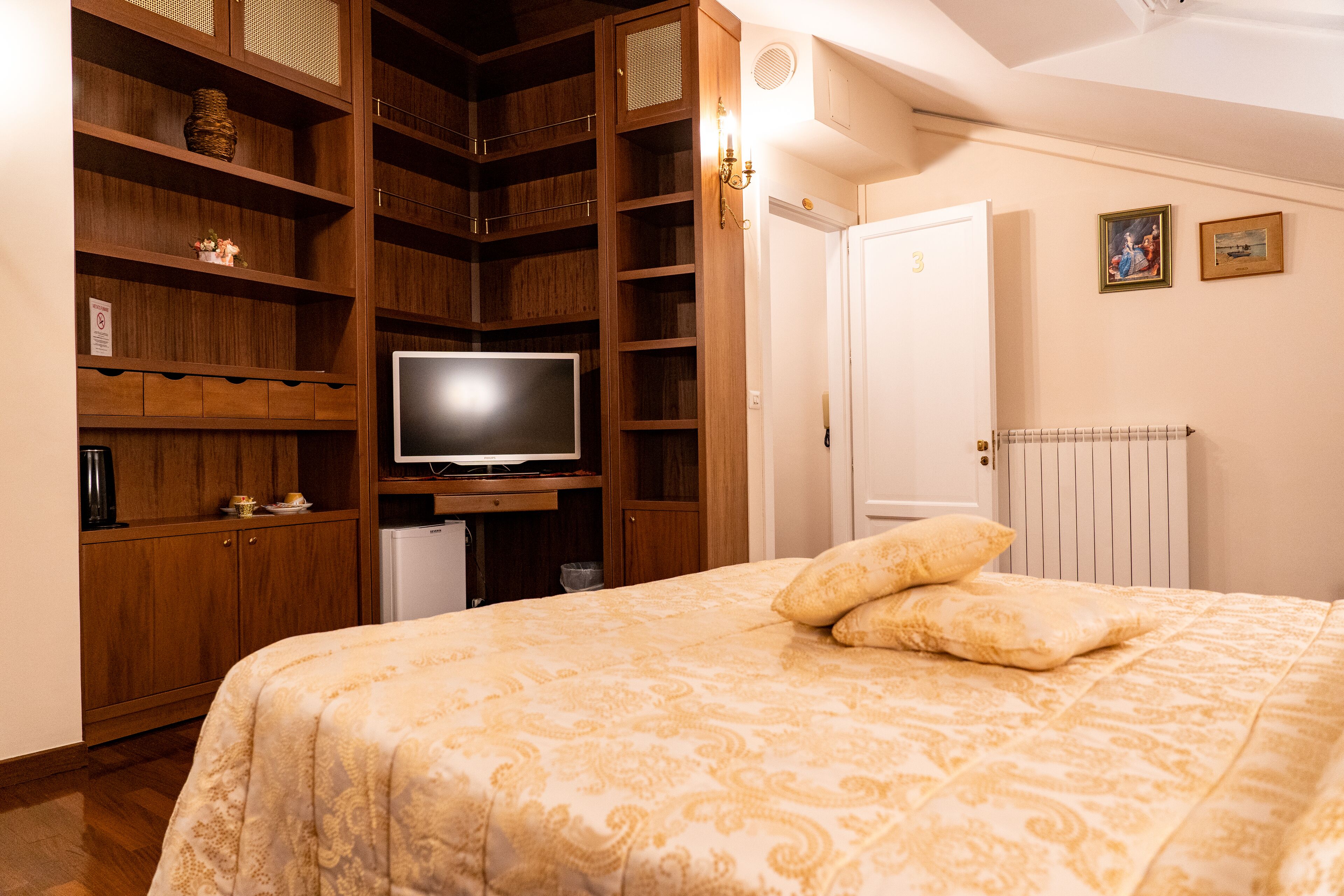 A bedroom with a large bed, wooden shelving, a television, and a white door.