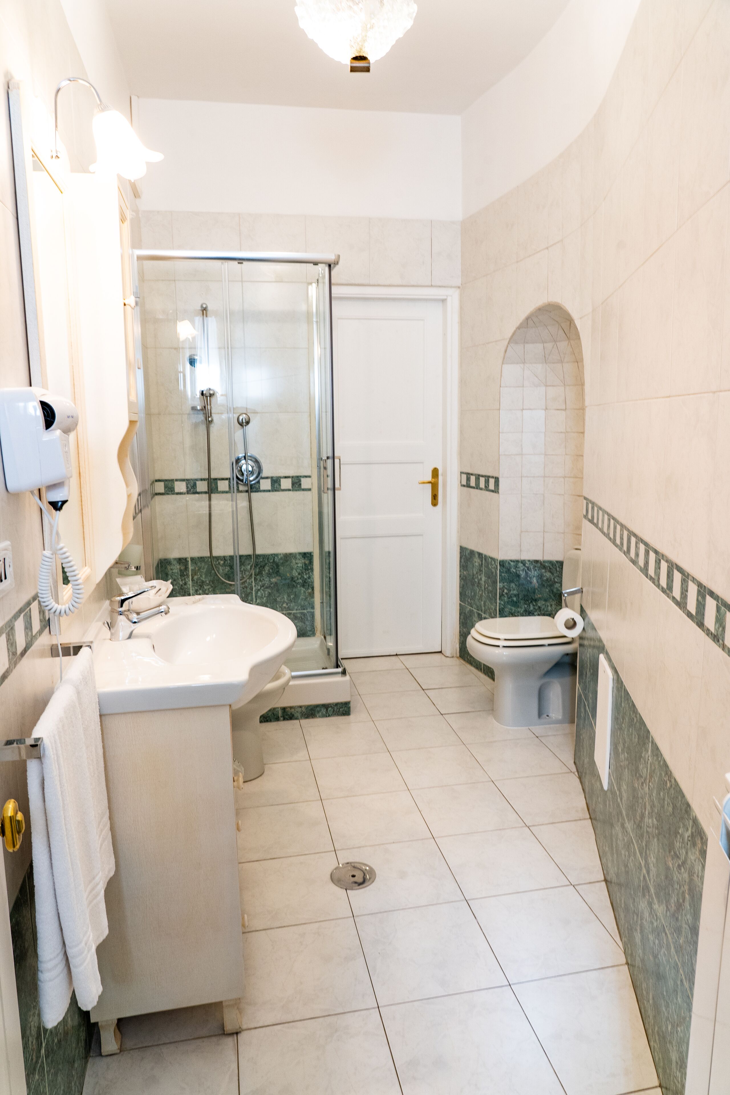 A bathroom with a shower, toilet, sink, and a hairdryer on the wall.