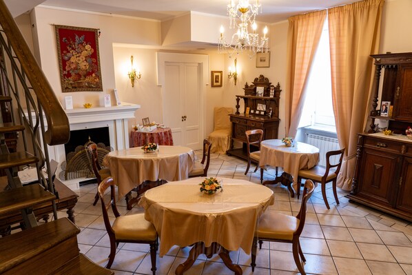 A dining area with round tables, chairs, a chandelier, and a fireplace. - Real Borbone (Caserta)