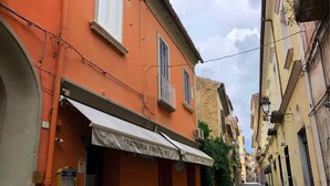 A narrow street with buildings on either side, including a shop with a sign that reads "TRATTORIA O'MASTO 1970". - Real Borbone (Caserta)