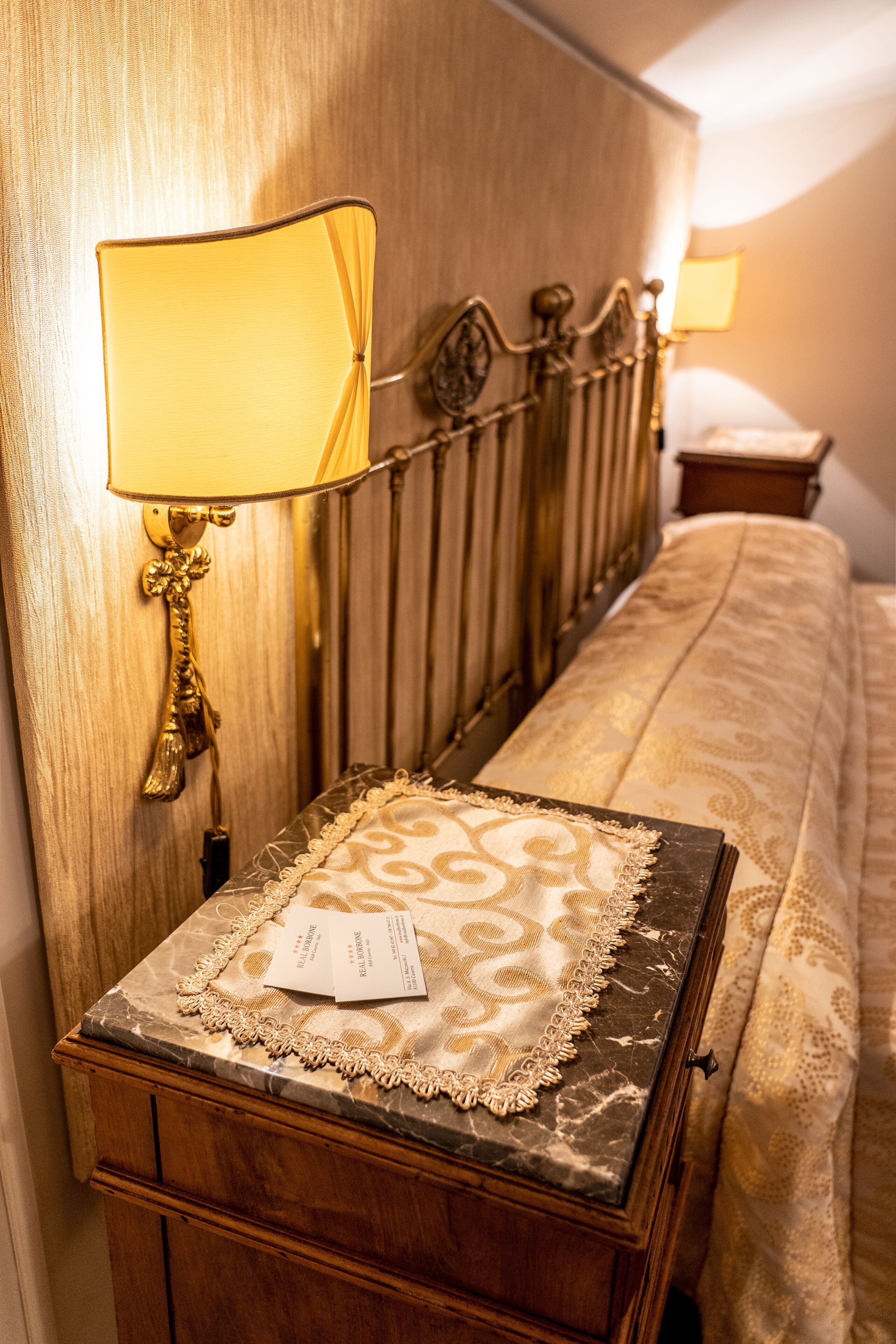 A neatly made bed with a patterned bedspread, a bedside table with a lamp, and a wooden headboard.