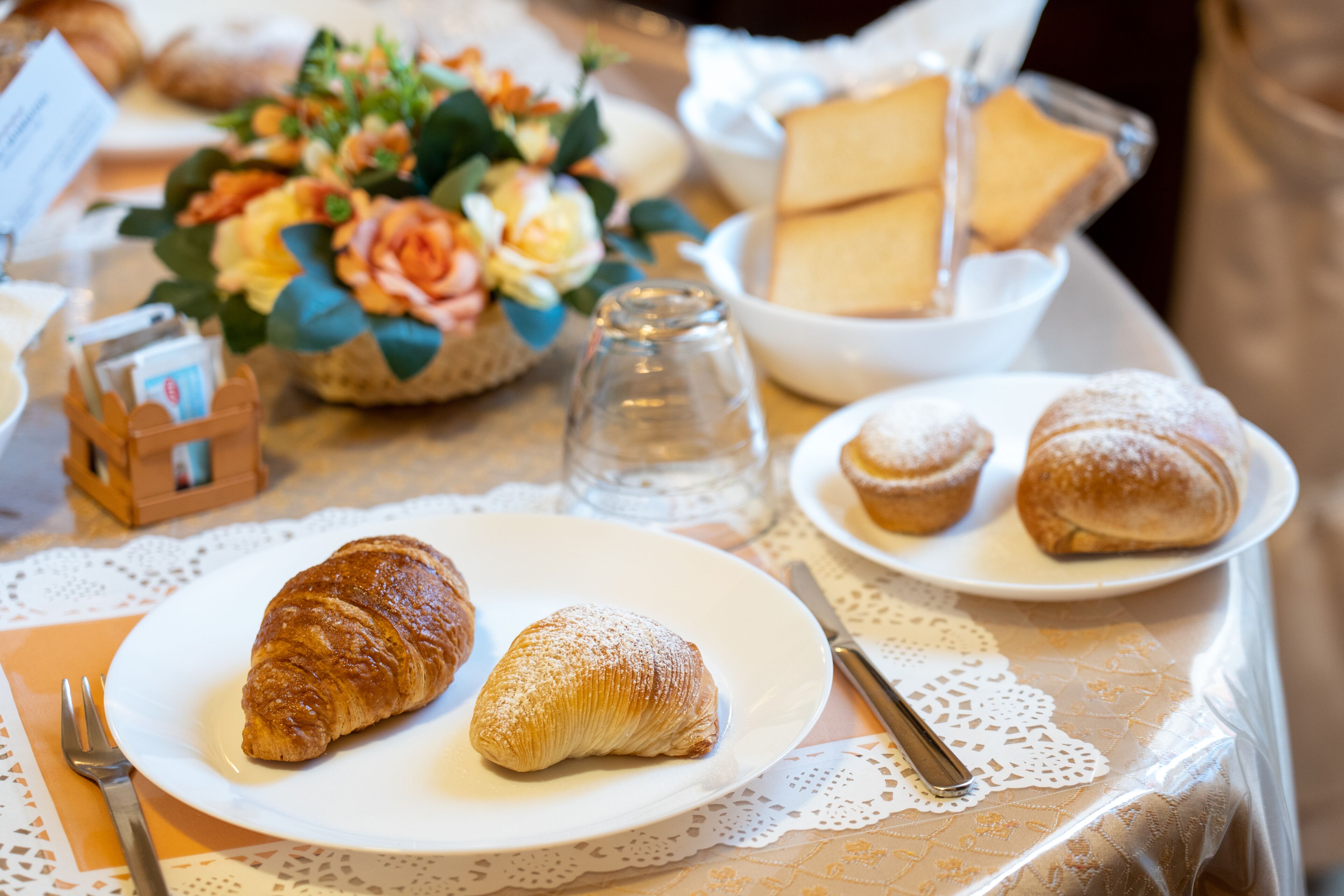Una mesa con croissants, un vaso de agua y un centro de mesa floral.