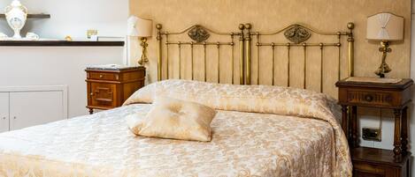 A neatly made bed with a patterned bedspread, a bedside table with a lamp, and a wooden nightstand with a mirror.