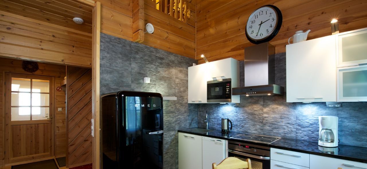 Uma cozinha moderna com paredes de madeira, uma geladeira preta, armários brancos e um relógio na parede.