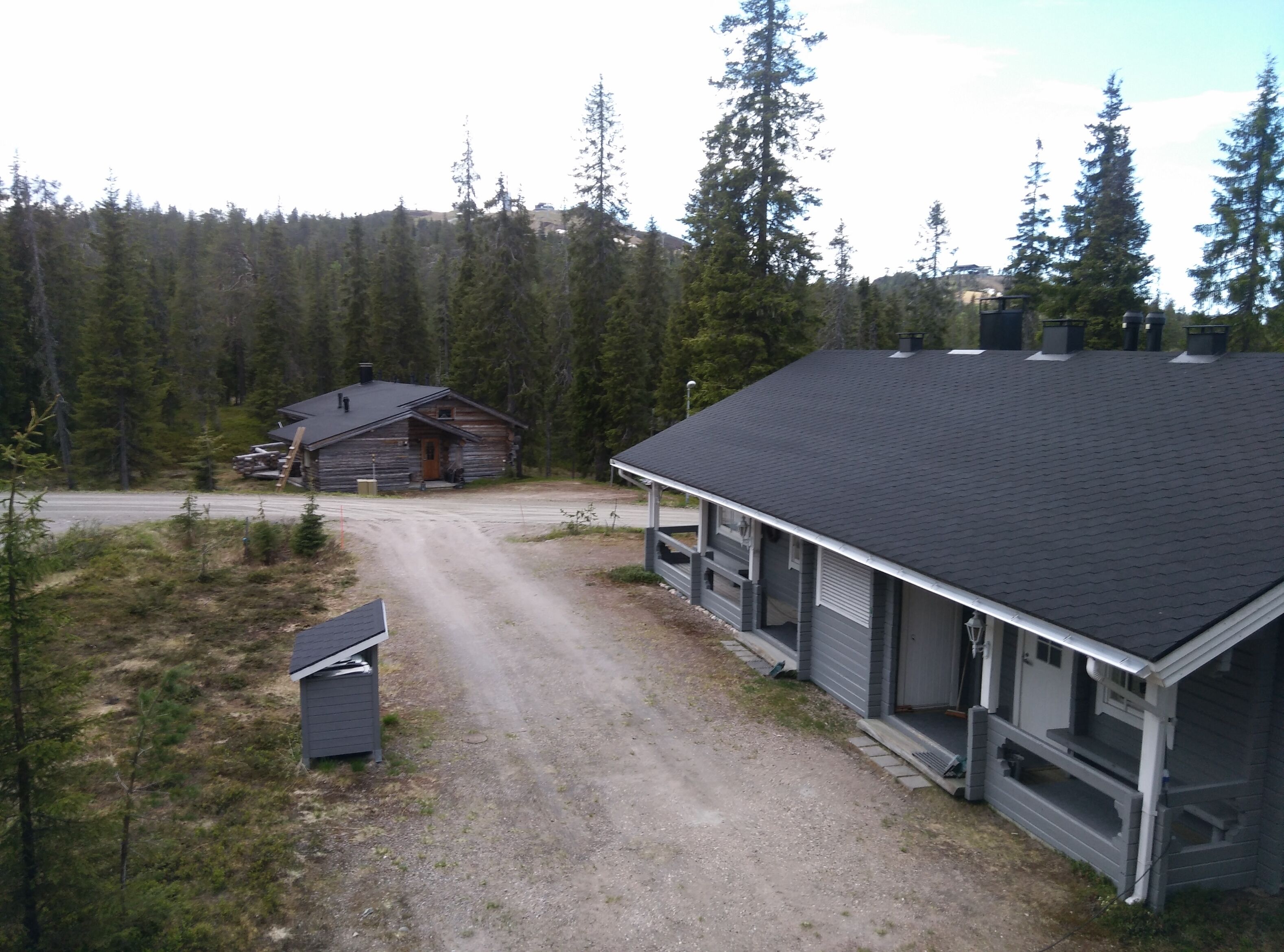 A cabin with a gravel driveway, surrounded by dense forest.