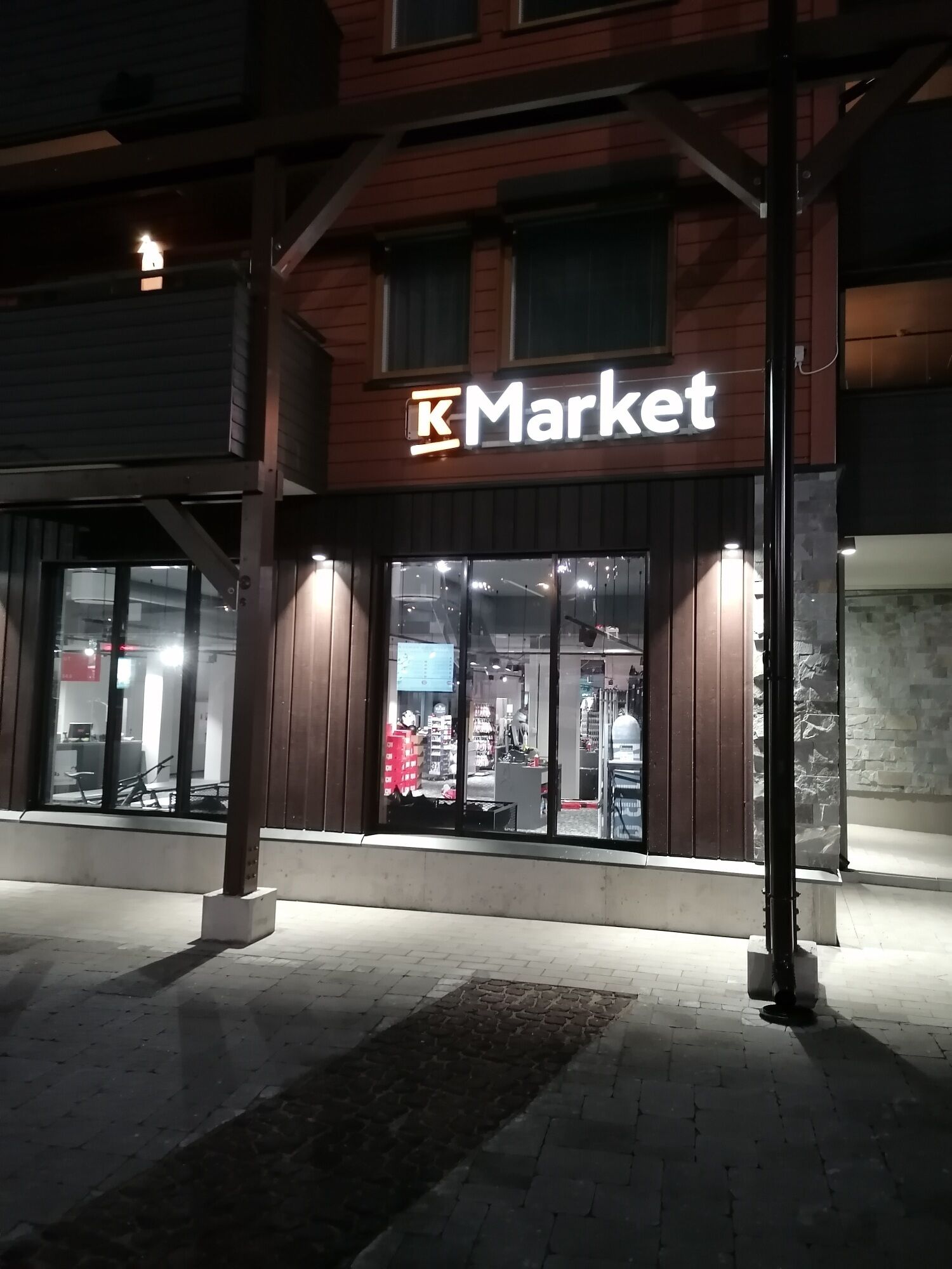 Un comercio Market iluminado por la noche, con letreros brillantes y grandes ventanales.