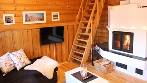 Un interior de cabaña acogedor con detalles de madera, una chimenea, un sofá con una manta de piel y un televisor montado en la pared.