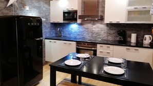 Una cocina moderna con refrigerador negro, armarios blancos, salpicadero de piedra y una mesa de comedor preparada para cuatro comensales.